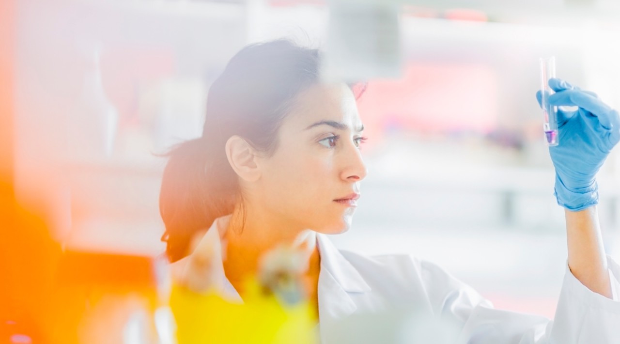 A photo of a woman in a lab coat looking at a test tube.