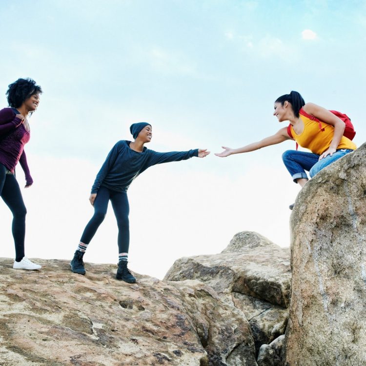 Woman helping friend hiking on rock formation